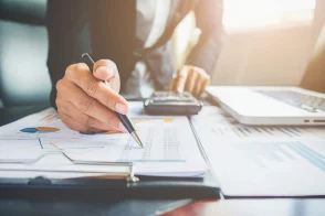 Personne en costume analysant des graphiques financiers avec une calculatrice et un ordinateur portable — illustration de la gestion de la pré-comptabilité.